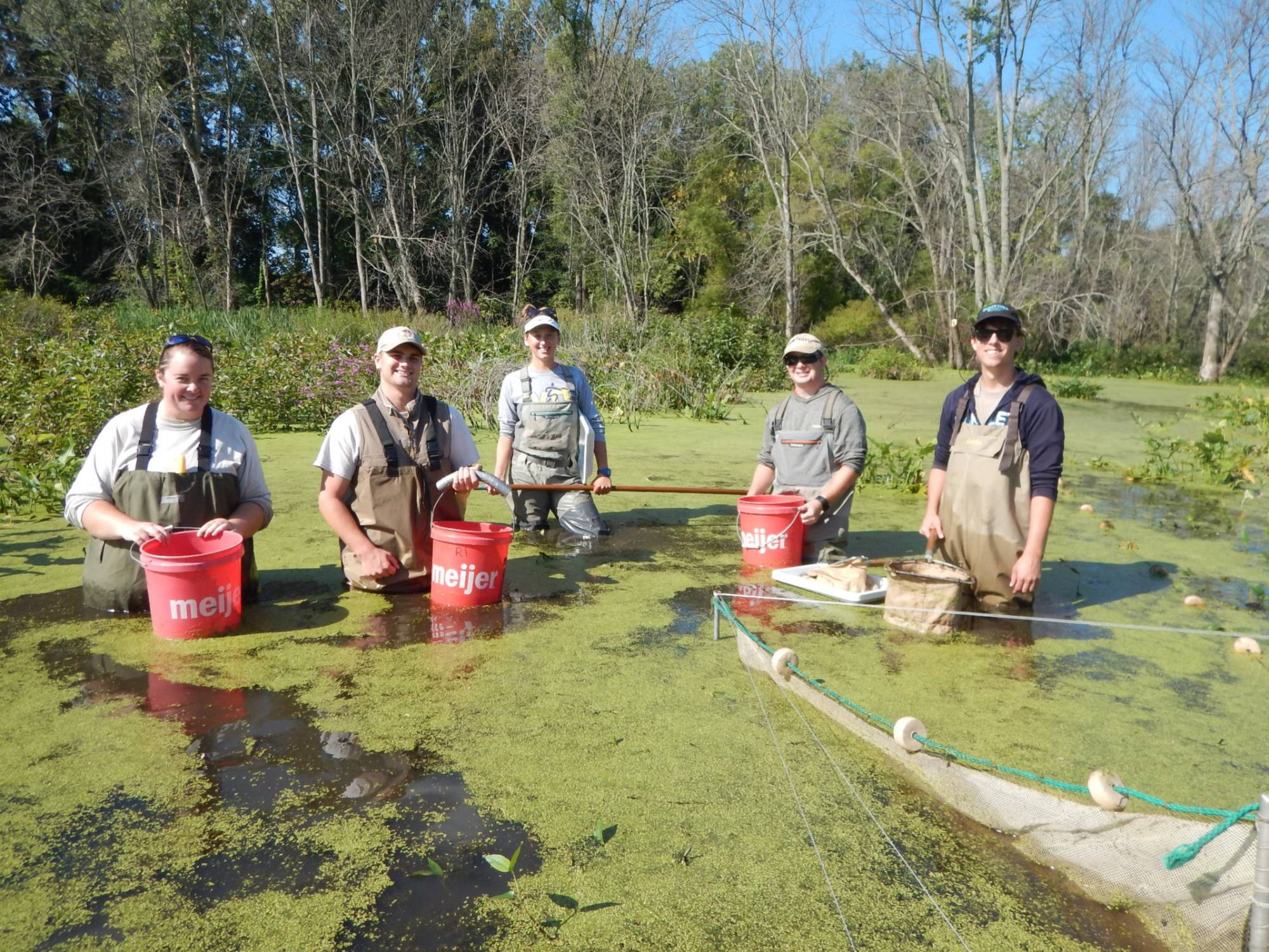 Dr. Ruetz and a group of technicians smile for a photo while waist-deep in a wooded lake covered by duckweed.